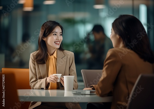 Two businesswomen talking and drinking coffee while sitting at table in office