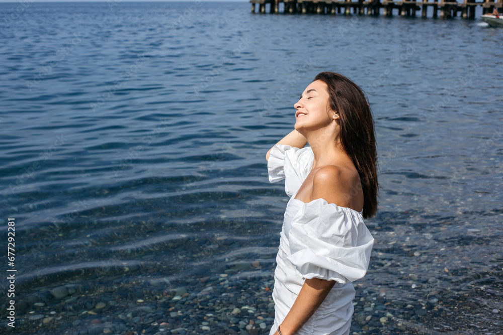 A girl straightens her hair while standing in the sea in the summer in a white dress