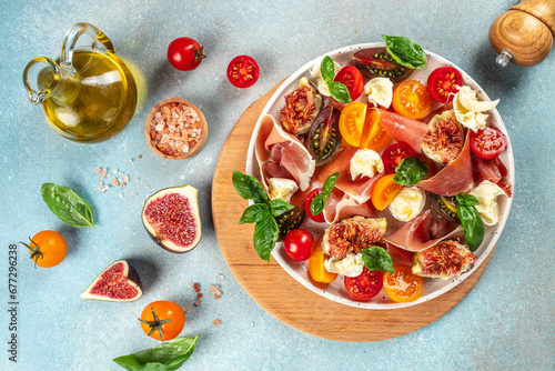 Fresh Salad with mozzarella, figs, prosciutto, fresh basil leaves and tomato on a light background top view