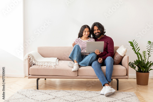 Happy indian lovers sitting on couch with laptop