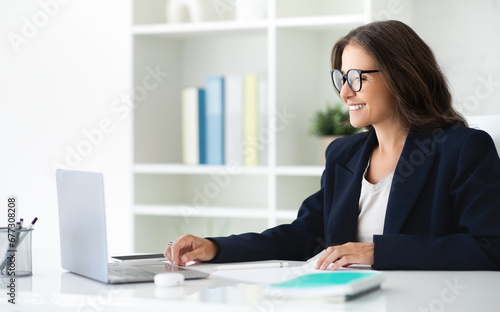 Positive mature woman manager using laptop at office