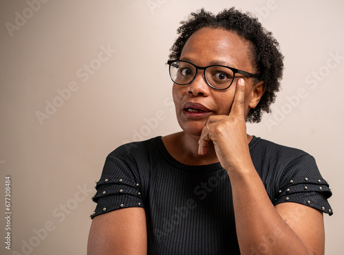 Black woman thinking with hand on face on pastel background.