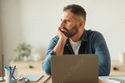 Depressed middle aged man sits troubled at laptop in office