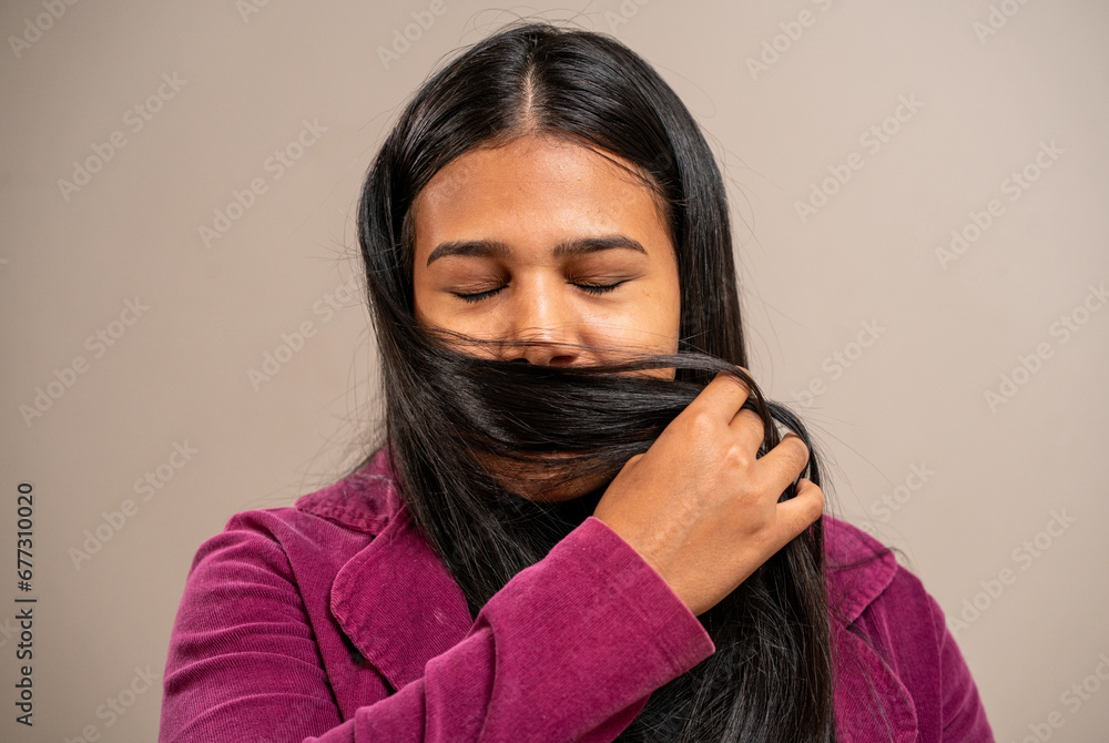 Obraz premium Young brunette woman with closed eyes smelling the perfume of her hair on pastel background.