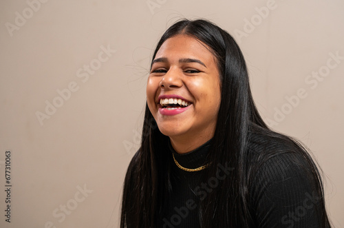 Young brunette woman with long hair laughing on pastel background.