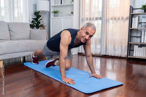 Athletic and active senior man doing exercise on fit mat with plank climbing at home exercise as concept of healthy fit body lifestyle after retirement. Clout