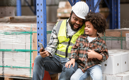 African father or dad hug his little son with love, smiling with happiness, wearing hard hat for safety, teaching, talking together while working in warehouse or factory. Education, Industry Concept.