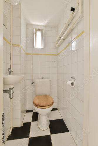 a small bathroom with black and white tiles on the floor  including a wooden seat in the toilet is next to the sink
