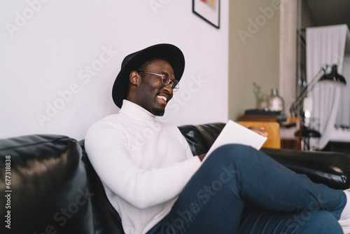 Happy black man reading textbook in living room