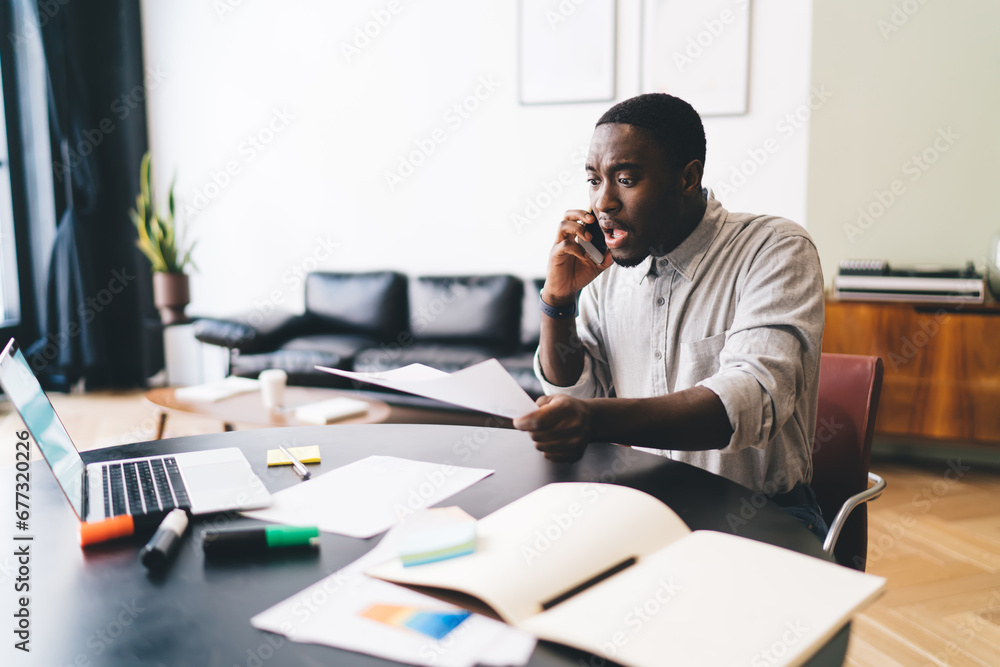 Upset black man speaking on smartphone at table Upset black man speaking on smartphone at table