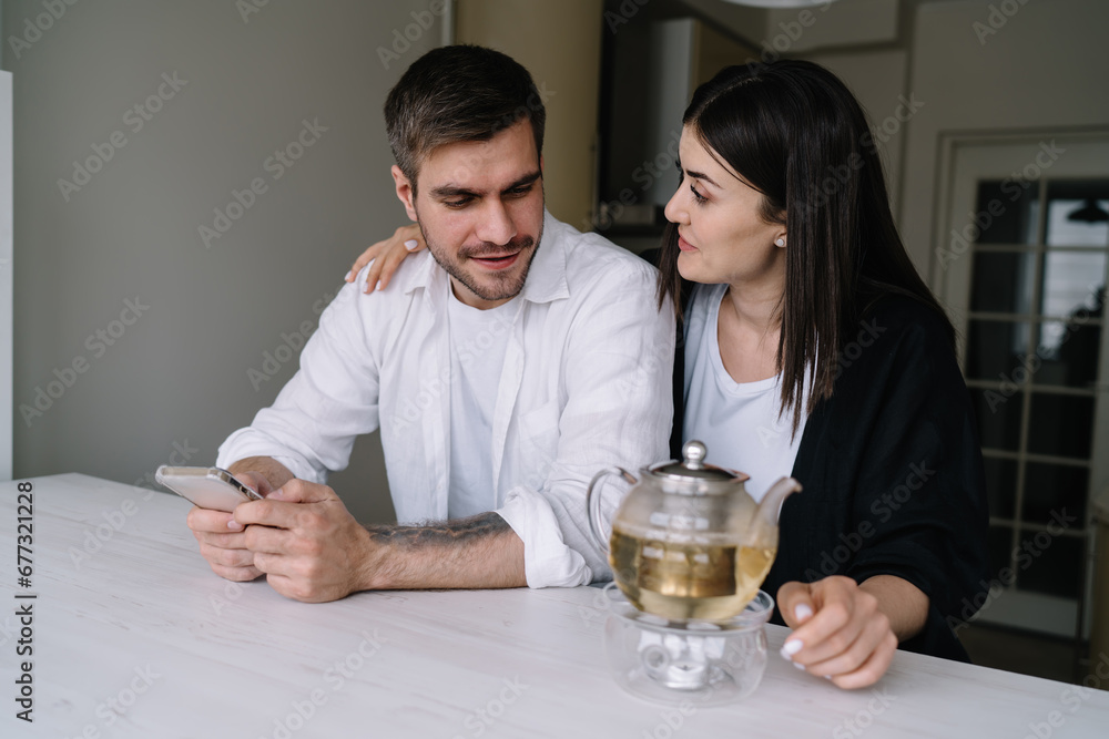 Happy couple using smartphone while sitting in kitchen Happy couple using smartphone while sitting in kitchen