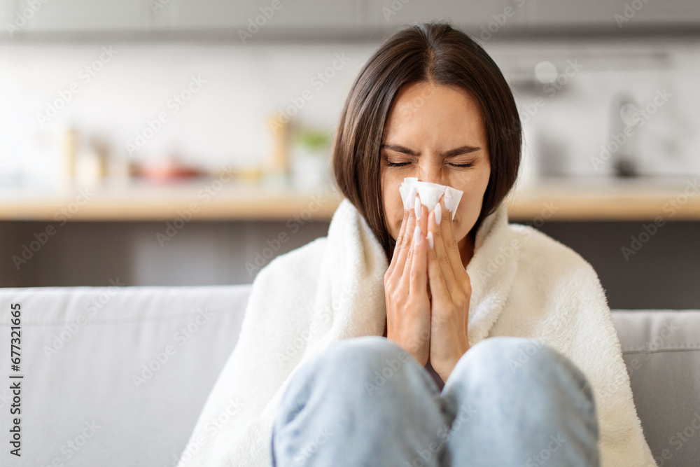 Sick Young Woman Blowing Nose In Paper Tissue While Sitting On Couch Sick Young Woman Blowing Nose In Paper Tissue While Sitting On Couch