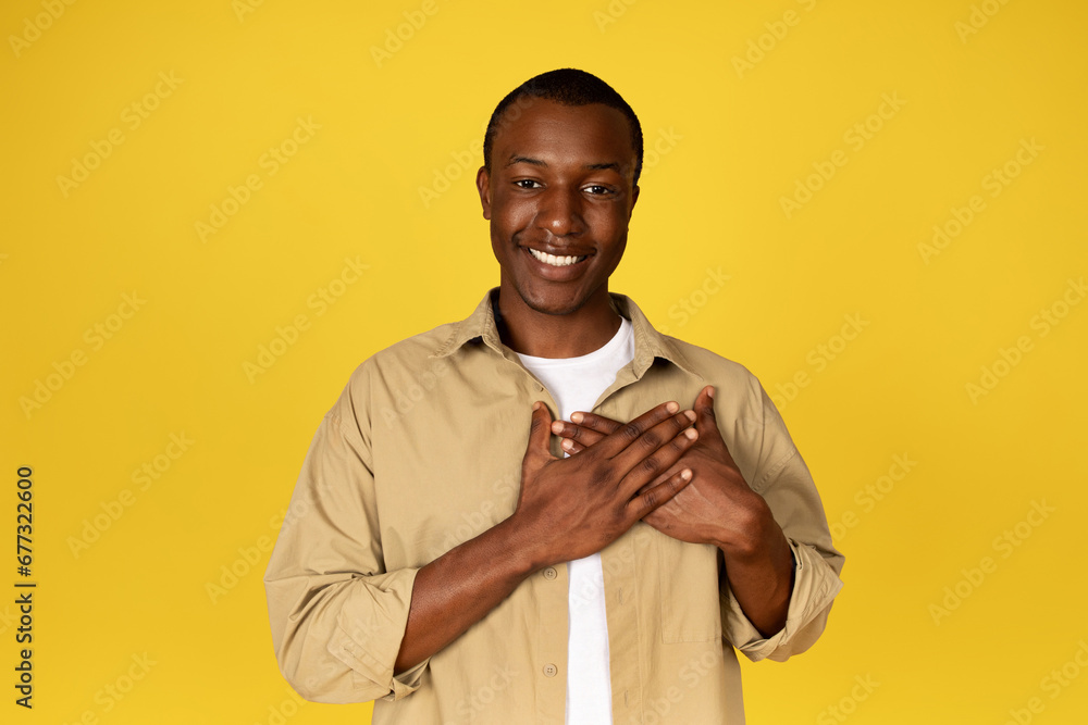 Glad handsome young black man presses hands to chest, enjoy good news