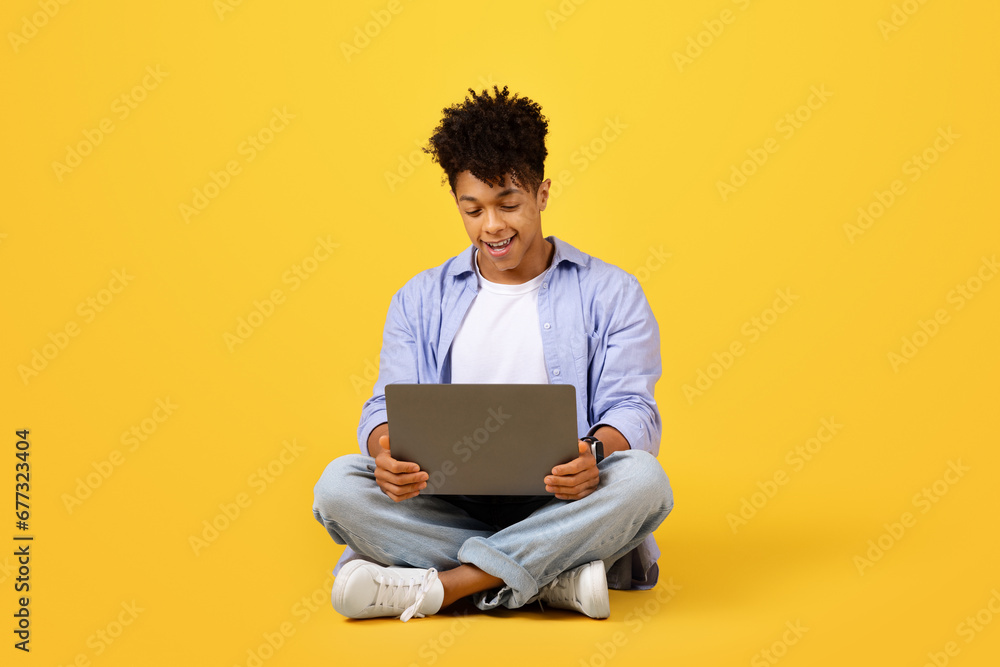Black man using laptop on yellow background Black man using laptop on yellow background
