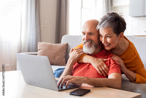 Smiling Senior Spouses Spending Time With Laptop In Living Room photo
