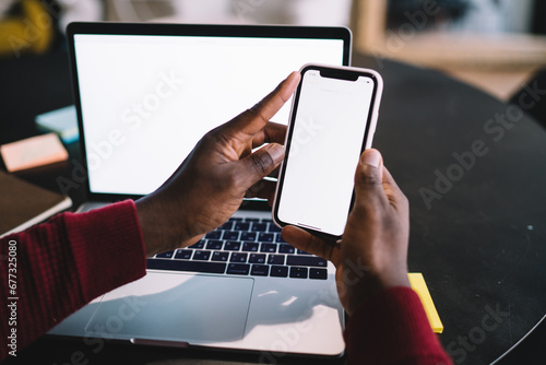 Unrecognizable black man with smartphone and laptop at table