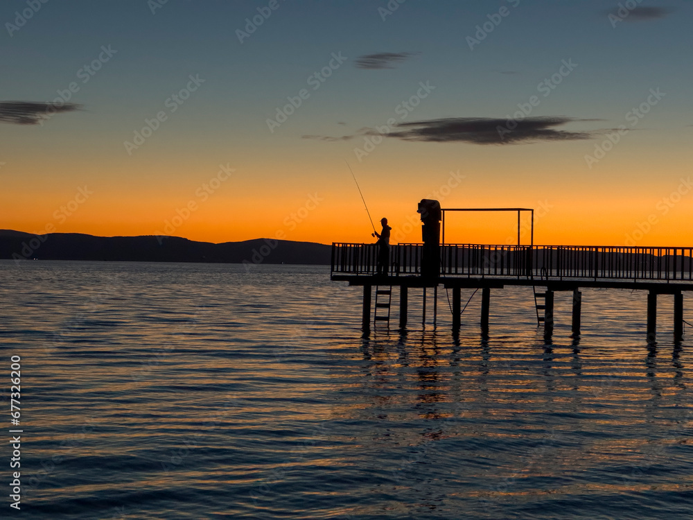 silhouette of the fisherman on the pier at sunset in the calm sea