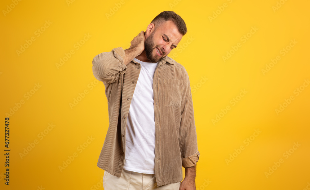 Unhappy millennial european man with beard in casual massaging neck with hand, suffer from pain Unhappy millennial european man with beard in casual massaging neck with hand, suffer from pain