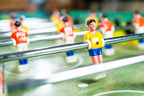 Scattered focus shot of table football game with red and yellow players and green plastic field, close up