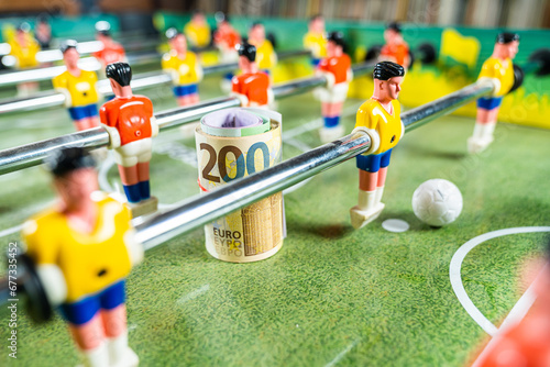 Blurred figures of plastic football players of table football game with euro bills, concept of sports industry investment