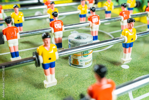 Table football game with roll of dollar bills in between plastic players, concept of betting and victory