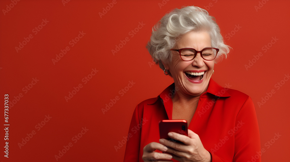 Happy senior woman smiling with her phone in a red background with space for text. Happy senior woman smiling with her phone in a red background with space for text.