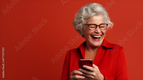 Happy senior woman smiling with her phone in a red background with space for text. 