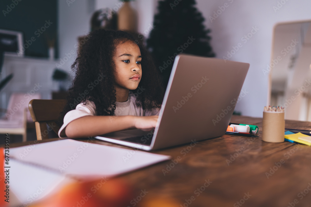 Thoughtful ethnic girl sitting at wooden table while working on laptop Thoughtful ethnic girl sitting at wooden table while working on laptop