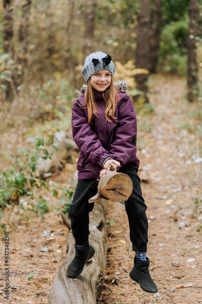 Photo, portrait, lifestyle of a beautiful smiling happy girl sitting on a log in the forest in autumn.
