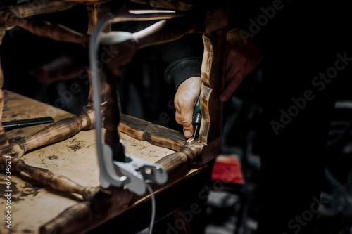 Male professional woodworker carpenter glues a chair, repairs furniture in the workshop. Photography, work concept, portrait.