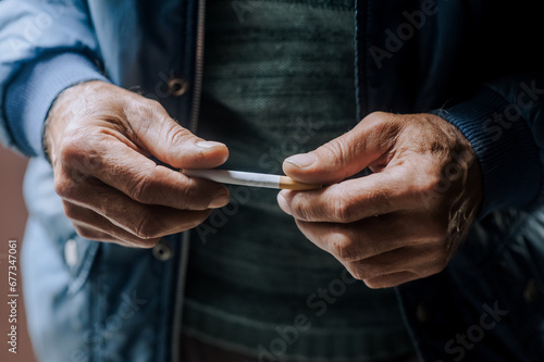 An elderly pensioner man is struggling with addiction, the desire to smoke, holding a cigarette in his hands. Medicine concept. Photography, close-up portrait.