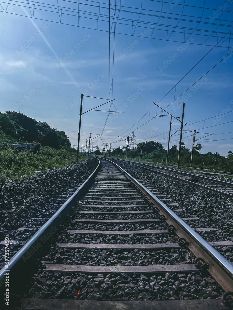 Vertical shot of the railway trails through a green field on a sunny day