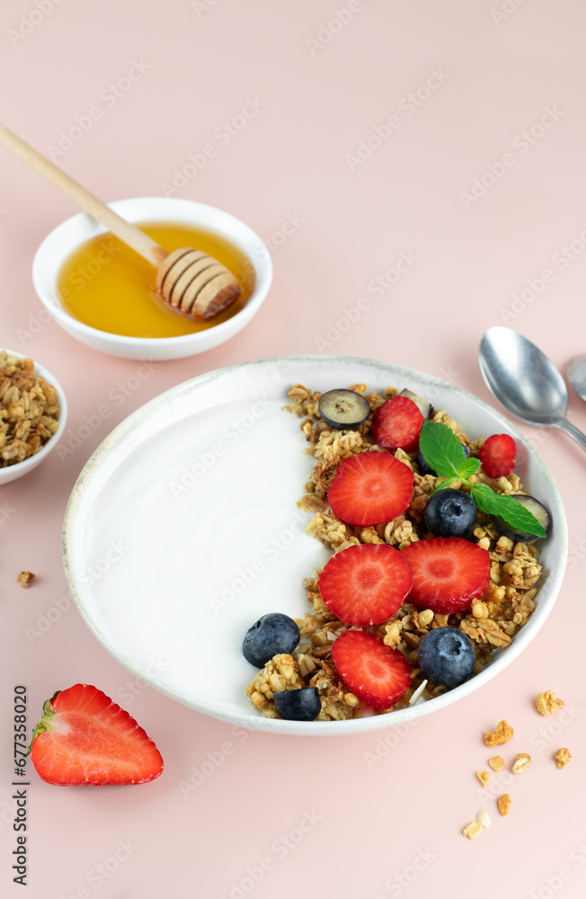Yogurt bowl with granola and fresh berries: strawberries and blueberries on a pink background. Top view. Yogurt bowl with granola and fresh berries: strawberries and blueberries on a pink background. Top view.