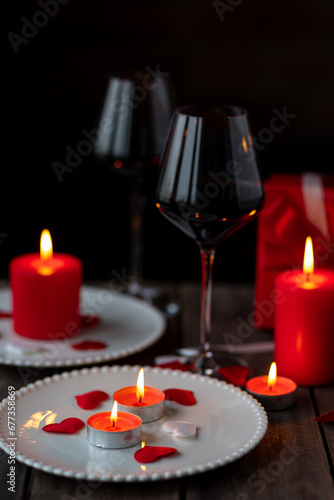 Saint Valentine s Day celebration. Red burning candles  hearts  gift box  postcard on dark wooden background. Happy holiday . Table decor for festive dinner  romantic atmosphere