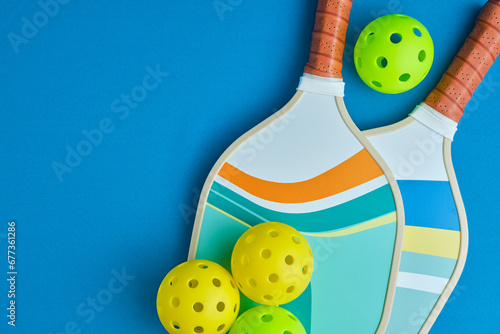 image from above of two pickleball paddles with three balls on a blue surface