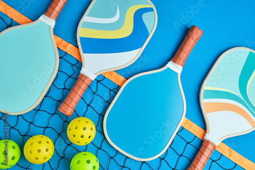 pickleball paddles in blue tones on top of a net on a blue background with three balls next to it
