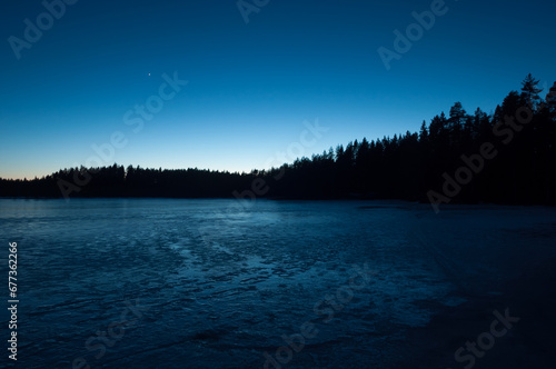 A small frozen lake in the forests of Finland in the blue light of evening