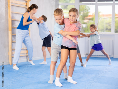 Purposeful engrossed children train during krav maga training session and work out basic elements with partner. Martial arts school, melee