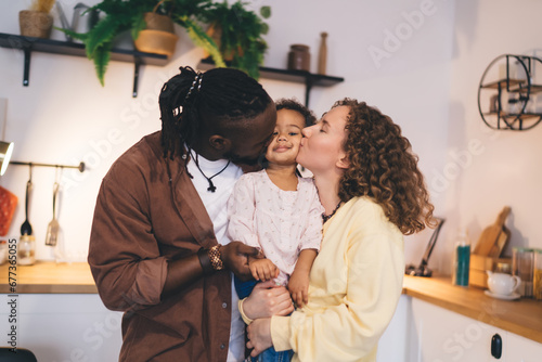 Happy diverse family with child kissing and hugging while standing near kitchen counter