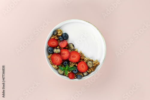 Yogurt bowl with granola and fresh berries  strawberries and blueberries on a pink background. Top view.