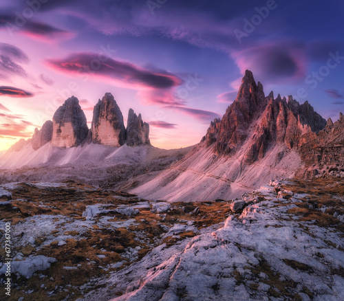 Alpine mountains at colorful sunset in autumn in Tre Cime, Dolomites, Italy. Colorful landscape with rocks and stones, trail, orange grass, purple sky with pink clouds at twilight in fall. Nature