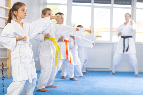 Kata karate teacher conducts classes and performs movements and fighting techniques together with boys and girls students to prepare them for competitions. © JackF