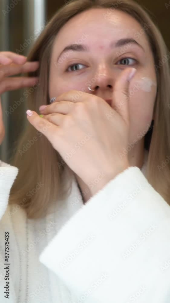 A beautiful and young girl in a bathrobe does morning self-care, dries her hair with a hairdryer after a shower, in the morning in front of a mirror in the bathroom A beautiful and young girl in a bathrobe does morning self-care, dries her hair with a hairdryer after a shower, in the morning in front of a mirror in the bathroom