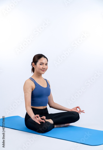 Asian woman in sportswear doing yoga exercise on fitness mat as her workout training routine. Healthy body care and calm meditation in yoga lifestyle in full body shot on isolated background. Vigorous