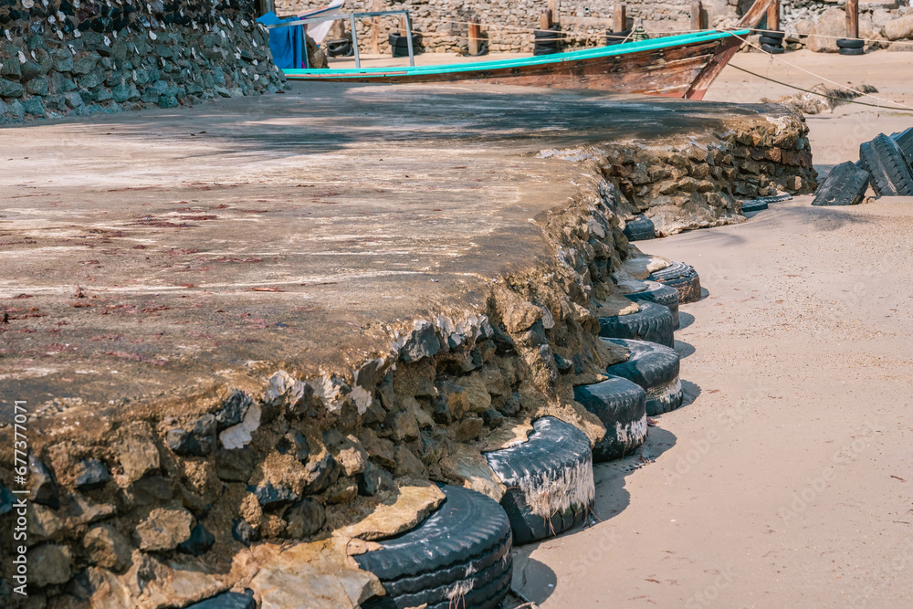 Old car tires used as for strengthening concrete sidewalk area built on sandy beach at high tide water level, perspective view - obrazy, fototapety, plakaty 
