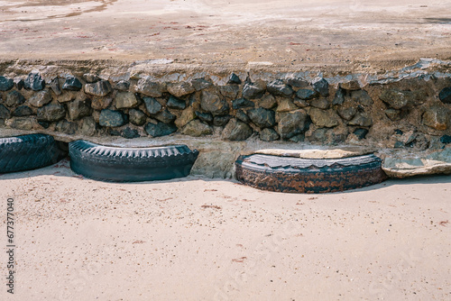 Old car tires used as for strengthening concrete sidewalk area built on sandy beach at high tide water level, front view