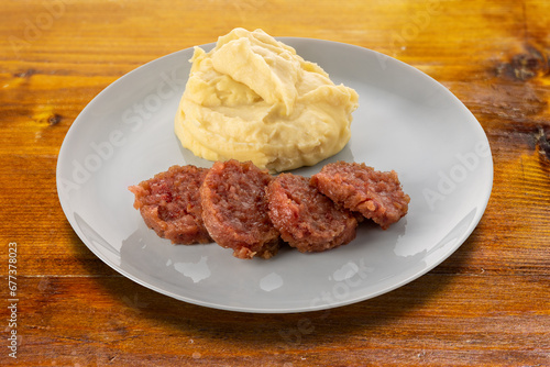 Slices of cooked sausage cotechino with mashed potatoes and sage leaves on plate on wooden table. Plate Cut out with clipping path included
