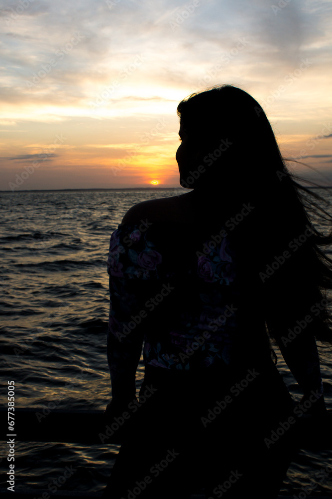 Silhouette of a woman watching the sunset on the beach with her hair moving in the wind breeze Silhouette of a woman watching the sunset on the beach with her hair moving in the wind breeze