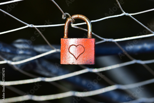 Vorhängeschloss rot mit Herz an einem Gitter befestigt, als Zeichen der Liebe.