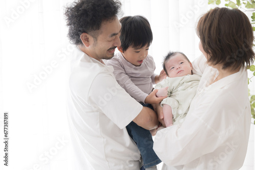赤ちゃんを抱くパパとママ　仲良し4人家族みんなでいい笑顔 コピースペースあり © kapinon